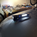 Customer photo of a Titanium Laser Pro flashlight with its side COB light on, lying on a car hood in a garage workshop