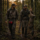Two hunters in camouflage walking through a forest, one carrying a red Blackout Survivor Radio emergency weather radio