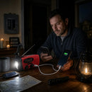 Man charging phone with Blackout Survivor Radio power bank during a home power outage with candles and a storm season sign in the background