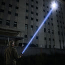 Man aiming the IRONCLAD X1 XL flashlight at night, beam reaching the top floors of a tall building
