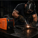 Welder using Mini Welding Machine ZX7-250 MINI on steel plate with sparks flying in dark workshop