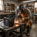 Welder in leather apron using Mini Welding Machine ZX7-250 MINI on metal frame in well-equipped workshop