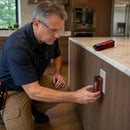 Electrician inserting NOYAFA NF-824 transmitter into a kitchen wall outlet with receiver resting on countertop nearby
