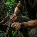 Survivalist using the WOLFSTRIKE D2 Survival Knife to cut thick rope in a dense jungle environment
